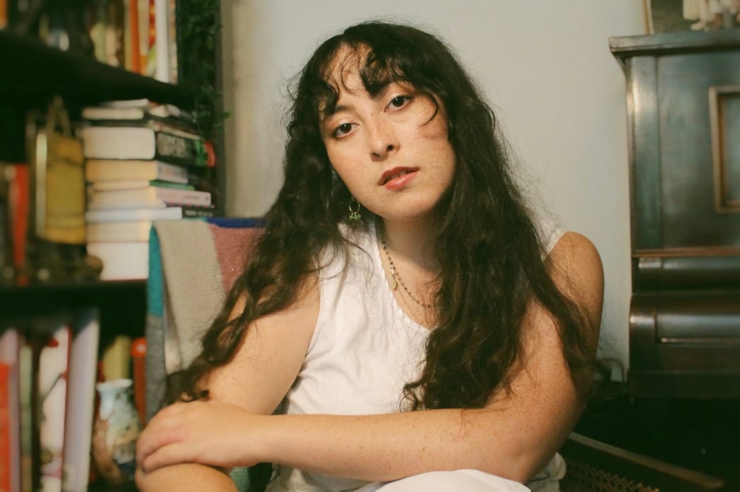 This photo shows the London-based singer/songwriter Ella Tobin in probably her home, with a bookshelf as backdrop, the artist