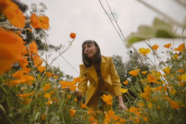 Photo of LA singer/songwriter, yoga instructor & wellness advocate little luna in an all orange flower bed.