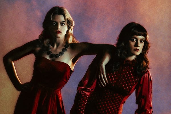 Photo of Australian singer/songwriter sister duo Charm of Finches: Ivy and Mabel Windred-Wornes in red dresses with expressiv