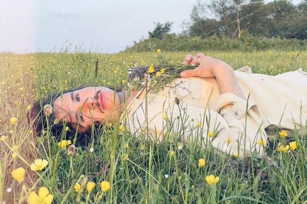 Portrait of Welsh singer/songwriter Tom Jenkins, laying in a blooming field looking directly in the camera, inviting the view